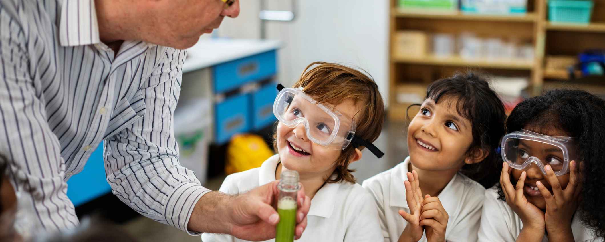 Een leraar laat een proefje zien aan kinderen in een klas. De kinderen kijken aandachtig mee.